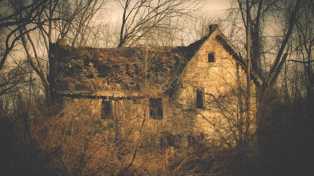 Old stone house with a damaged roof and empty openings among trees.