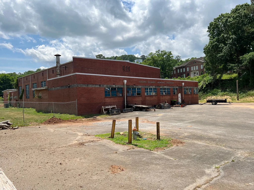 Abandoned old brick gymnasium with shattered glazing and benches and equipment left outside its facade.