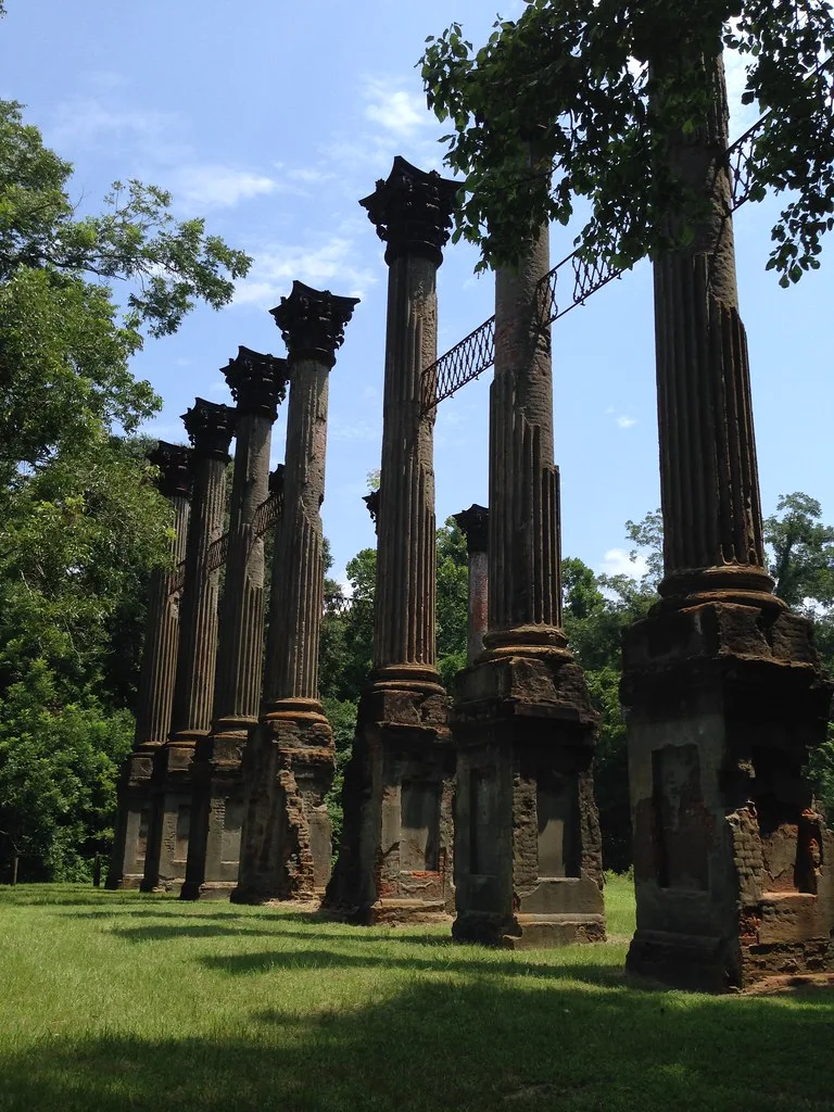 Row of ruined columns in a tree-lined area.