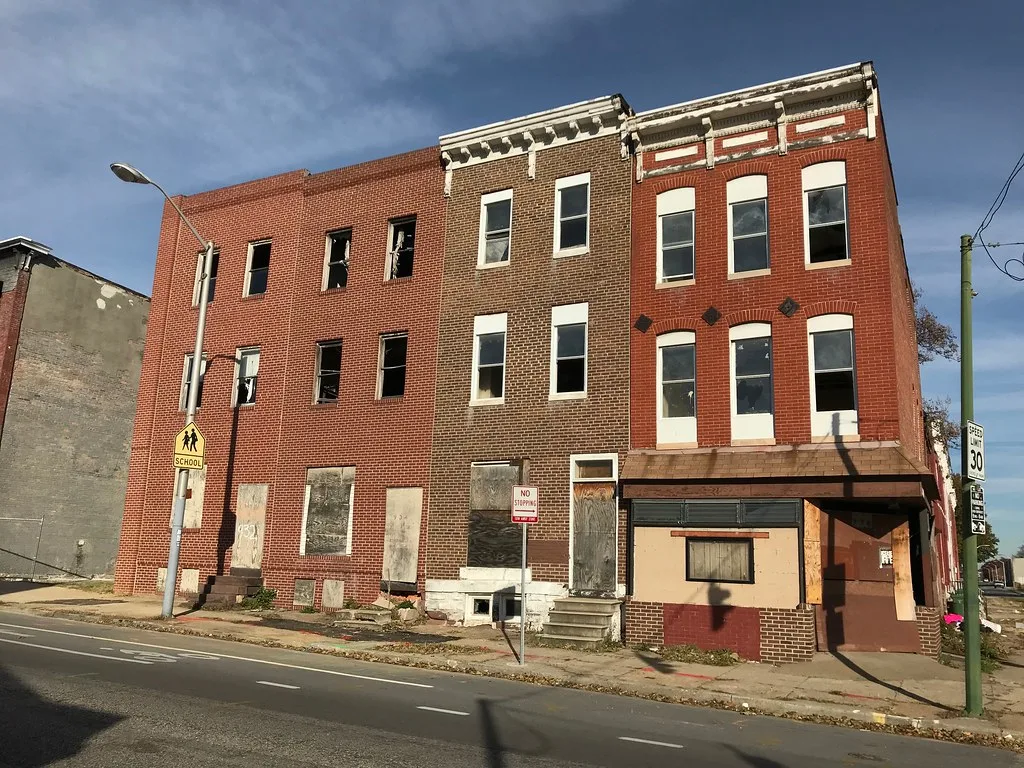 Row of red brick buildings with broken windows and boarded ground floors.