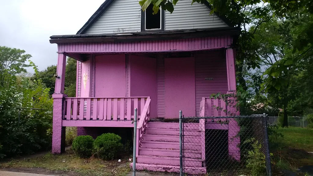 Abandoned house with a pink-painted porch and boarded openings.