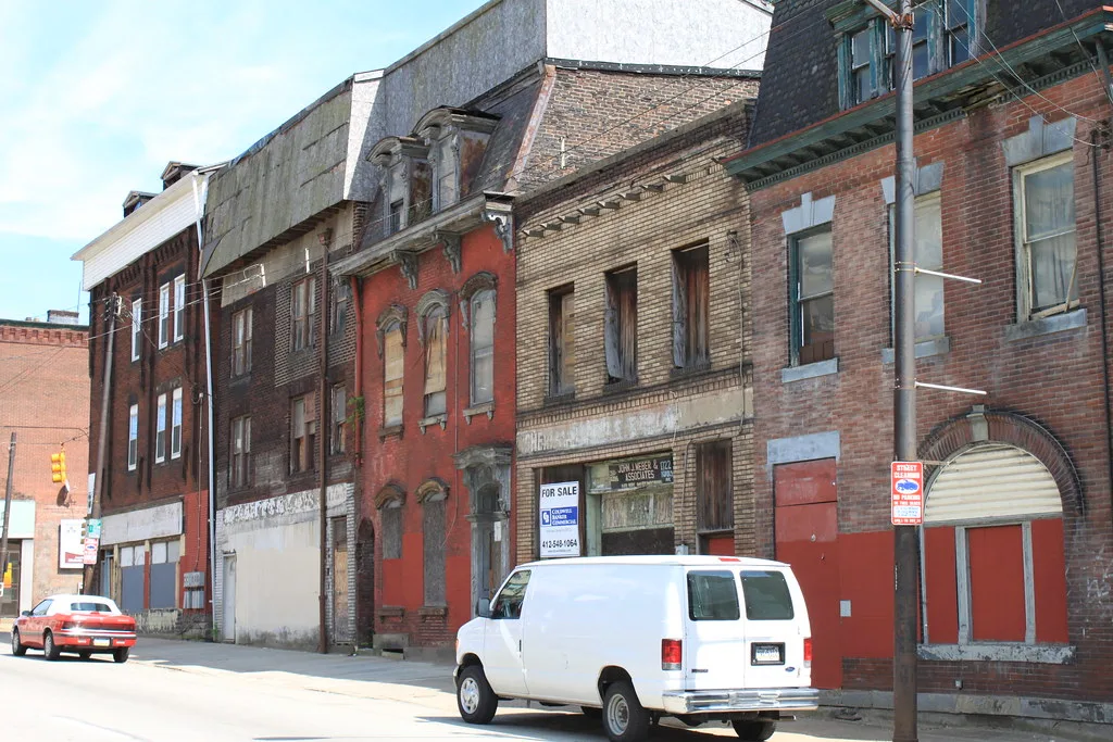 Old urban facades with boarded openings behind a van.