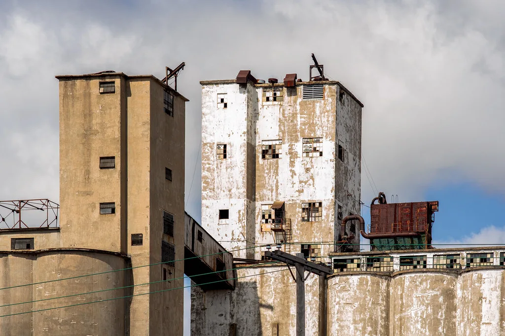 Towers of a neglected industrial plant with broken windows and flaking white paint.