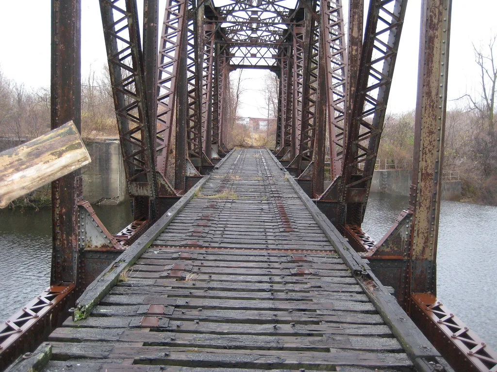 Old metal railway bridge with weathered sleepers above water.