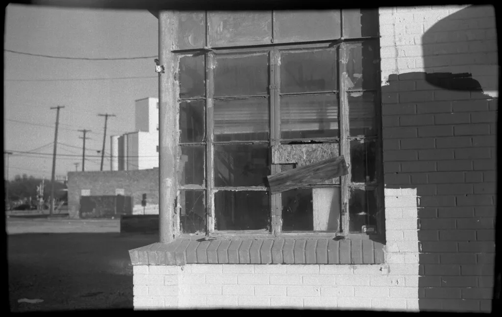 Broken industrial window partly closed with boards, in black and white.