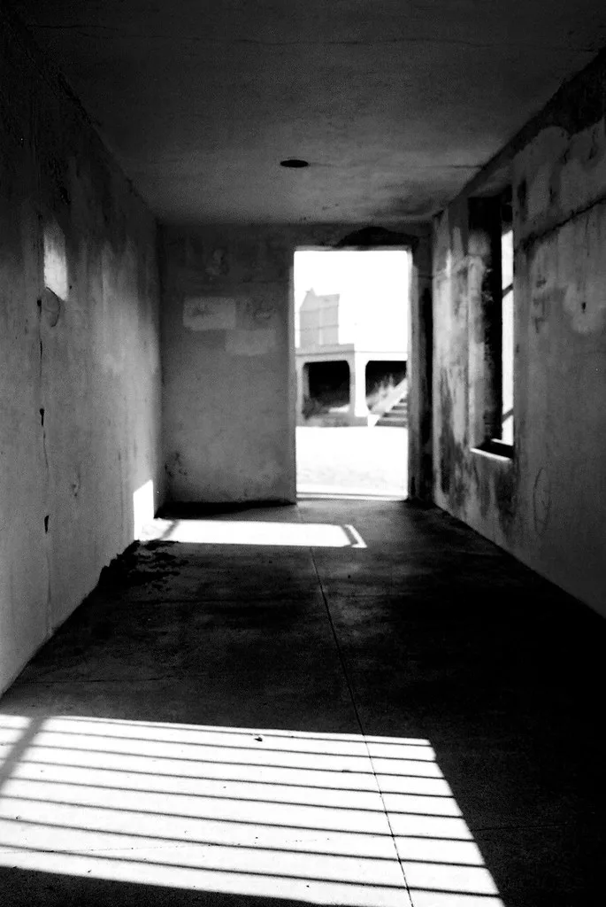 Pièce vide aux murs abîmés et à la fenêtre sans vitrage, en noir et blanc.
