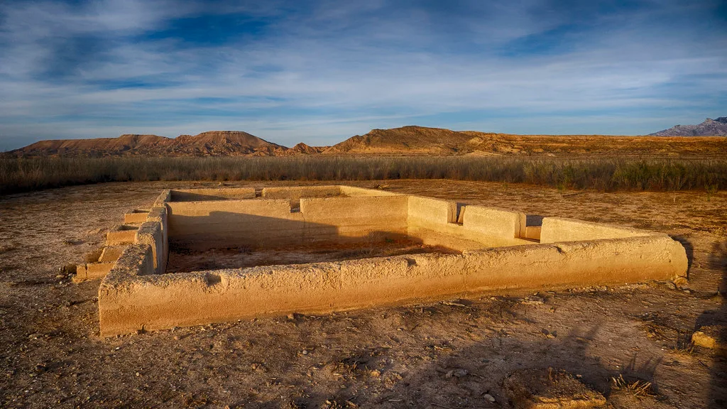 Low ochre wall remnants outlining a roofless room on an arid plain.