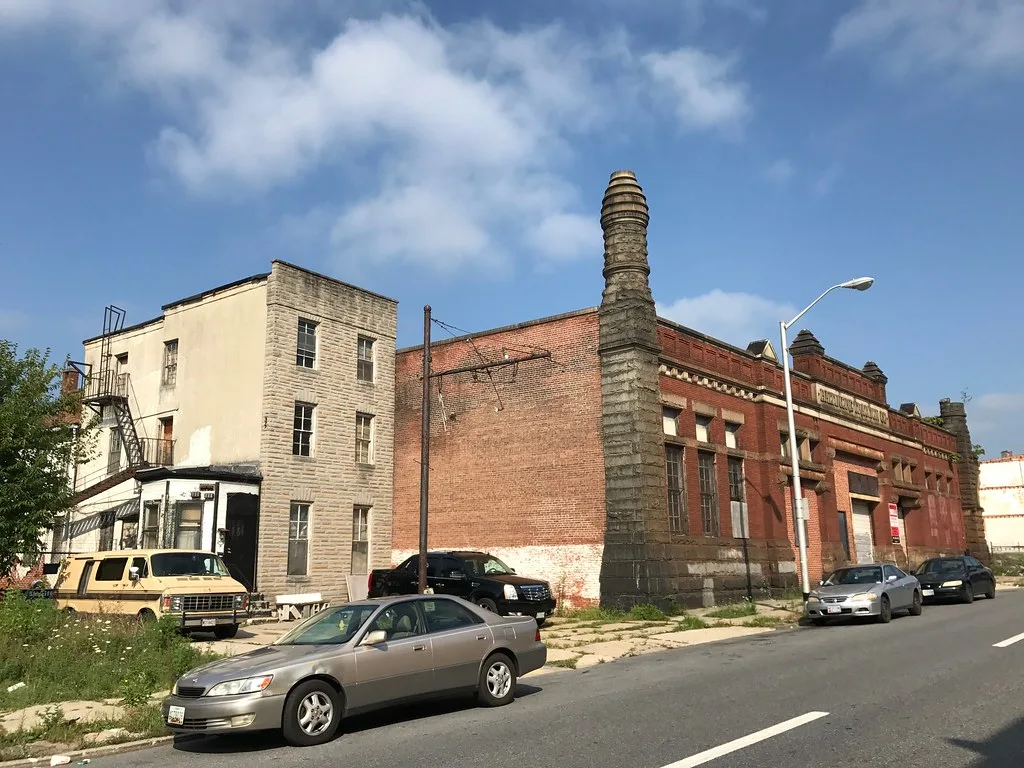 Old red brick power station with boarded windows beside a street.