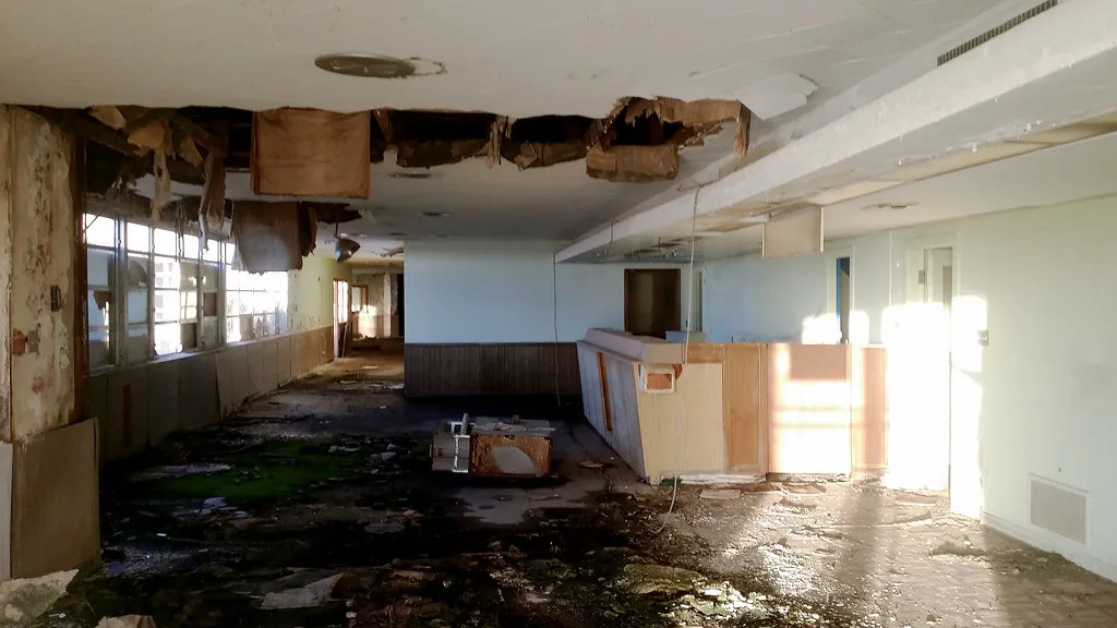 Ancienne salle d’aérogare dégradée avec un comptoir et un plafond effondré.