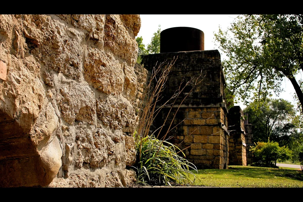 Old stone kilns with metal elements in a tree-lined setting.