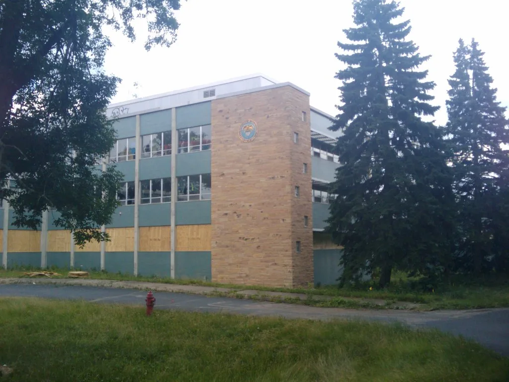 Abandoned three-storey building with green panels, broken windows and boarded ground-floor openings.