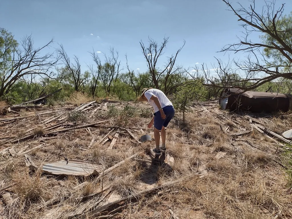 Timber debris and an old rusty tank in a dry overgrown site with a visitor in the foreground.