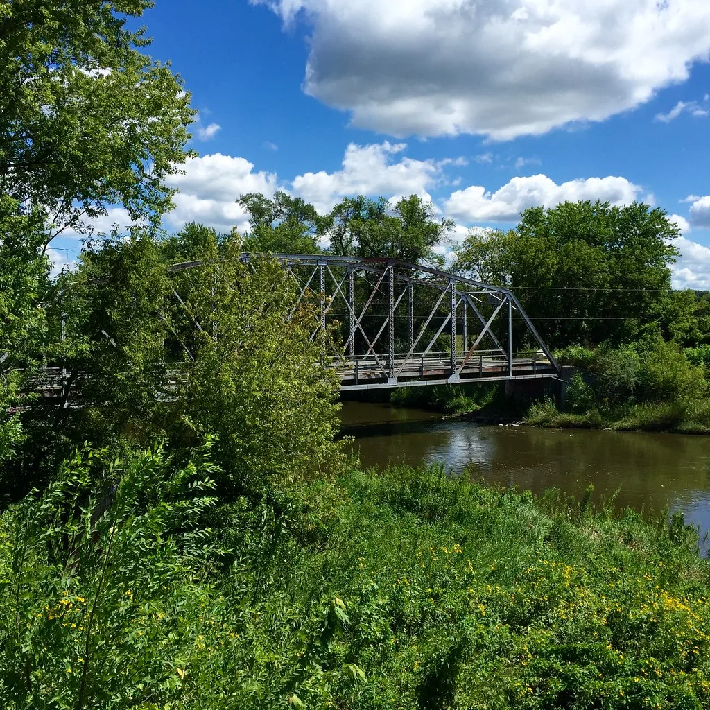Old metal truss bridge over a tree-lined river.