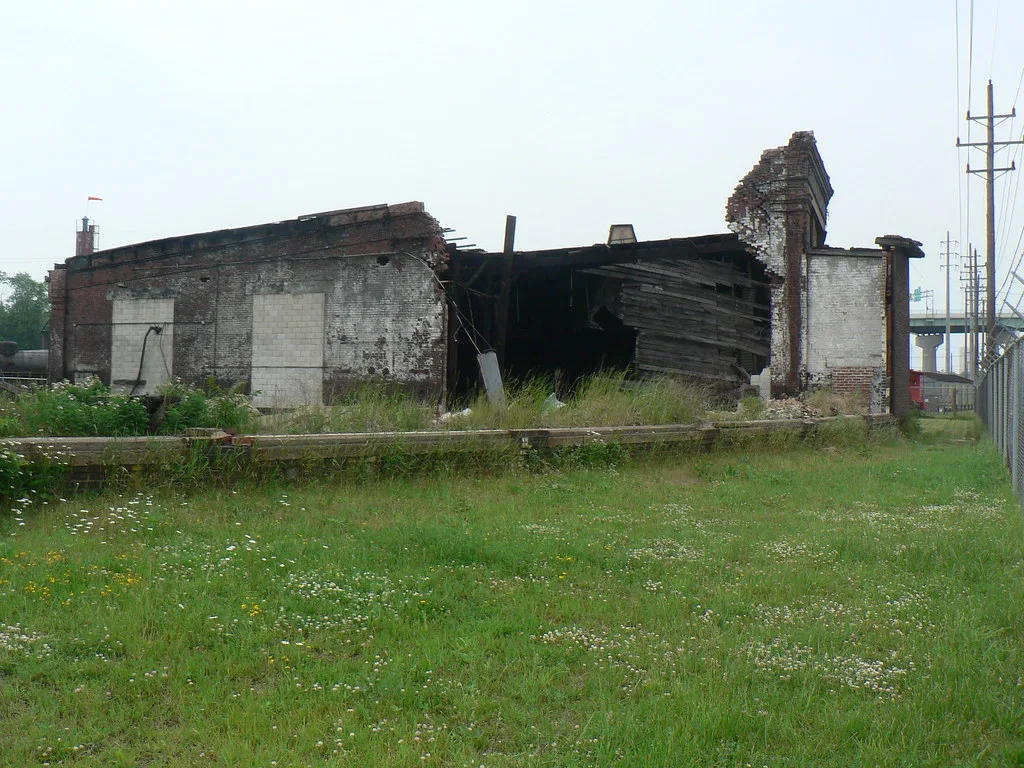 Bâtiment en briques partiellement effondré dans une prairie.