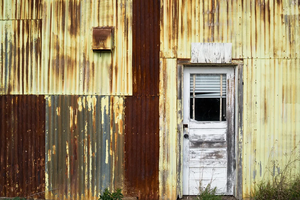 White door with a broken pane in a rusty yellow sheet-metal facade.