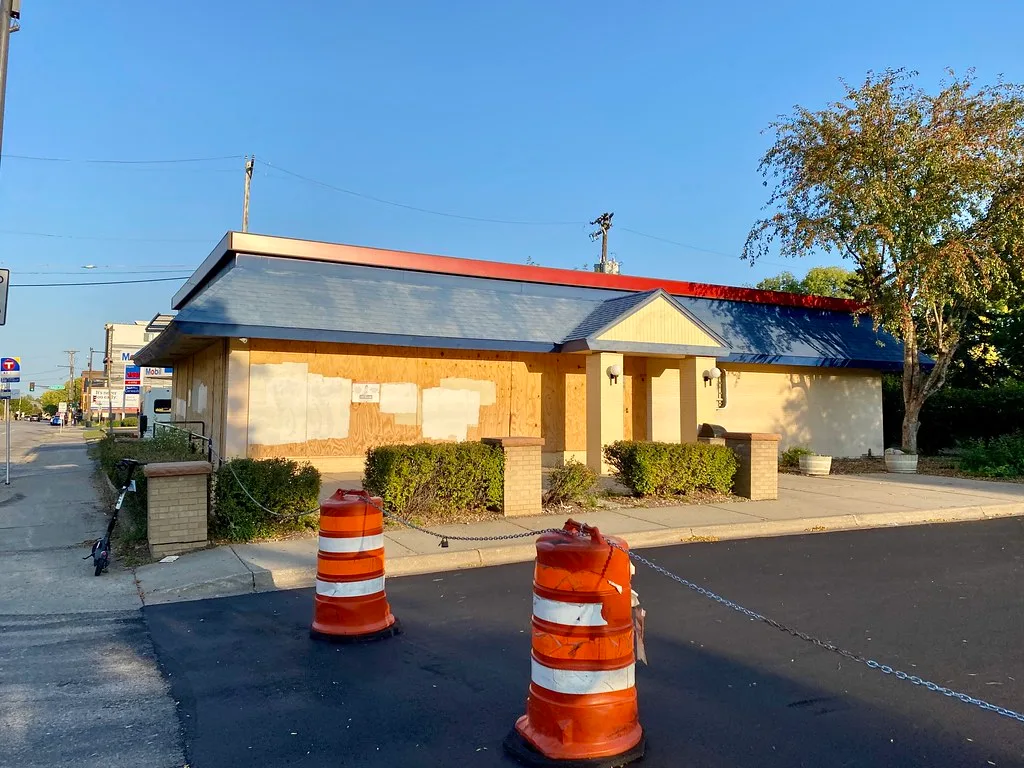 Old restaurant with boarded windows behind a chain and orange barriers.