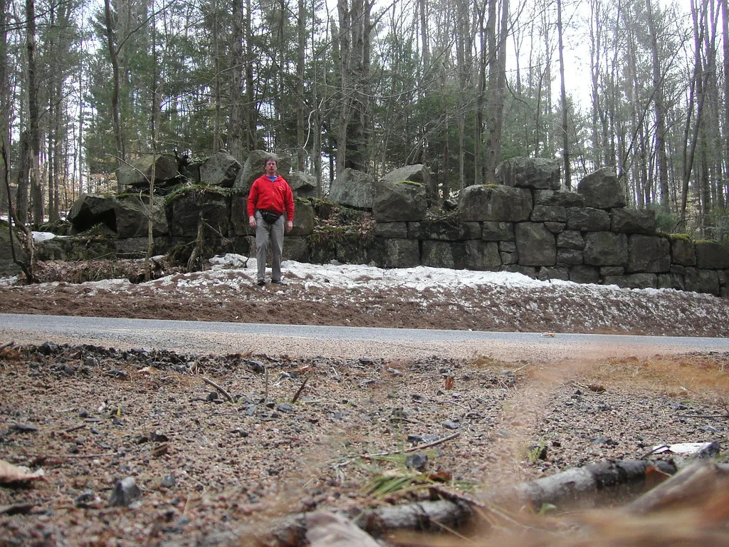 Vestige de mur en gros blocs de pierre sous les arbres, avec une personne devant dans la neige.