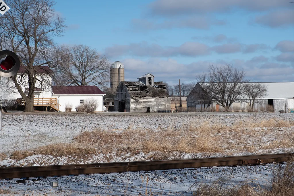 Old barn with a collapsed roof among farm buildings, in the snow.