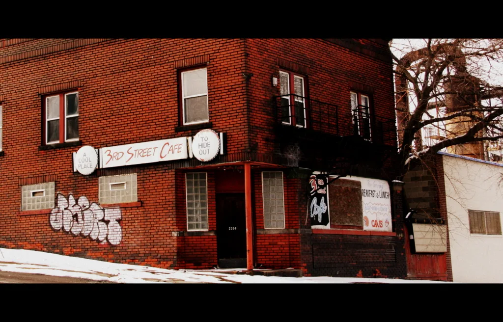 Closed graffiti-covered old brick cafe on a street corner.