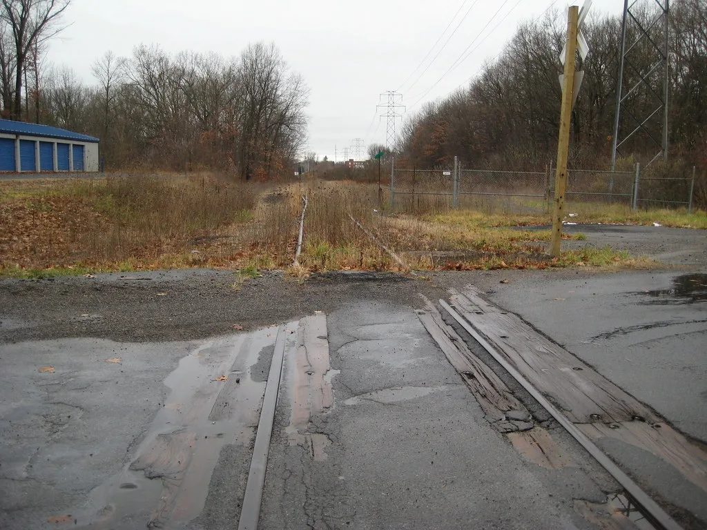 Old railway tracks overgrown with grass beyond a level crossing.