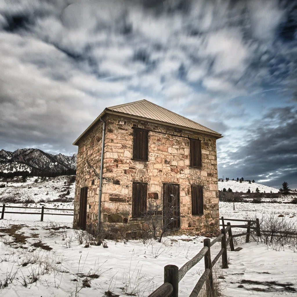 Small stone house with boarded openings in snow.
