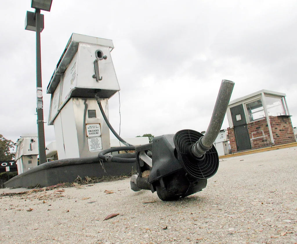 Fuel nozzle lying on the ground in front of old filling-station pumps.