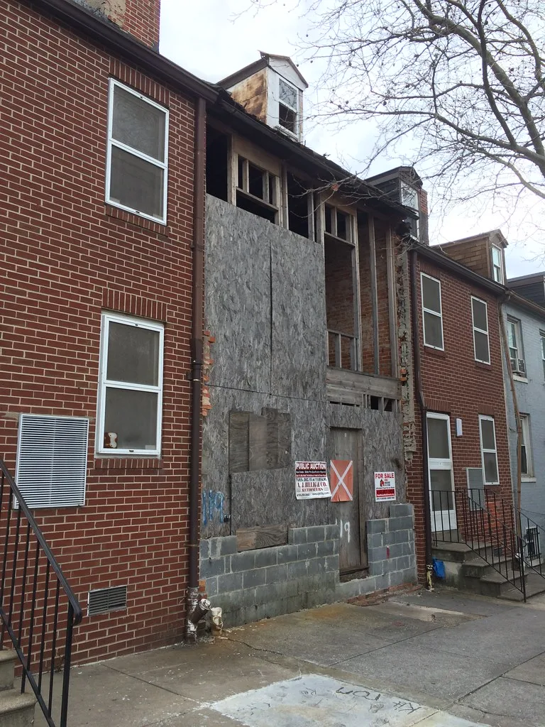 Abandoned row house with its facade stripped away and sealed with boards and concrete blocks.