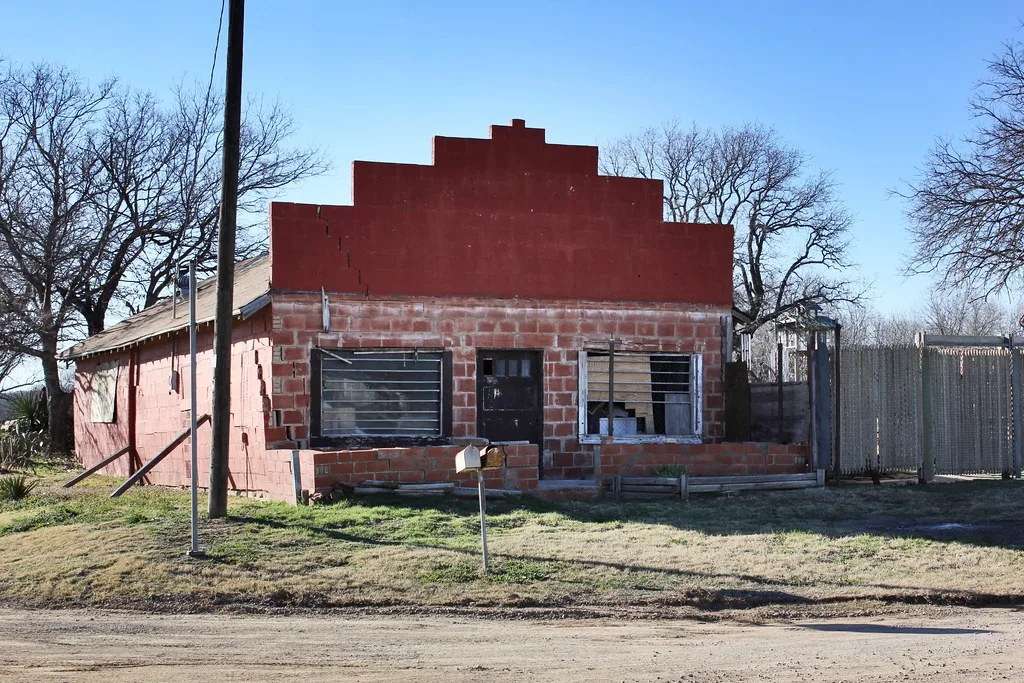 Ancien petit bâtiment commercial rouge aux fenêtres dégradées.