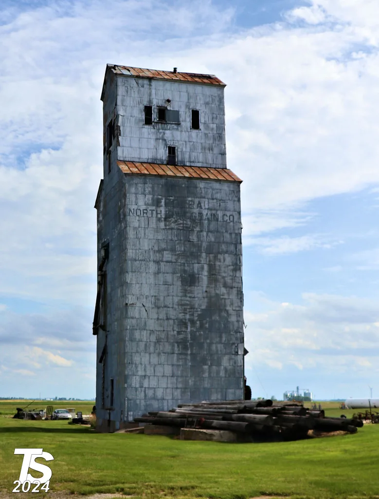 Old gray elevator with empty openings and a rusty roof.