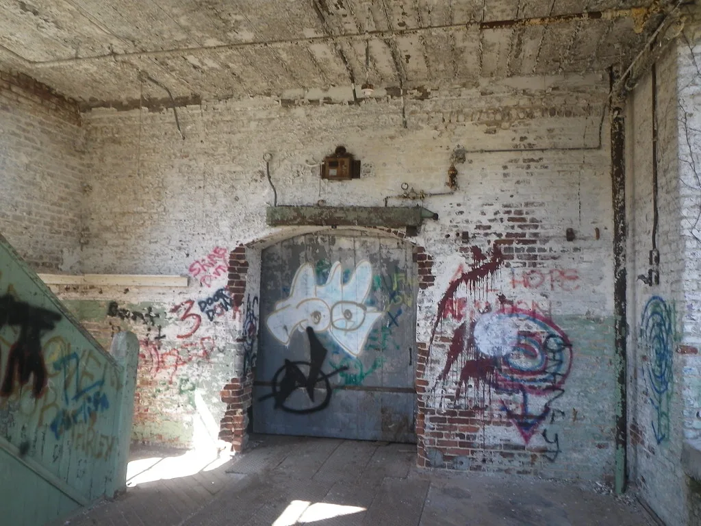 Old graffiti-covered metal door in a dilapidated brick room.