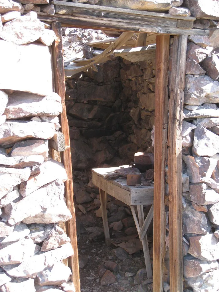 Wooden doorframe opening into a stone room with a broken roof and dusty workbench.