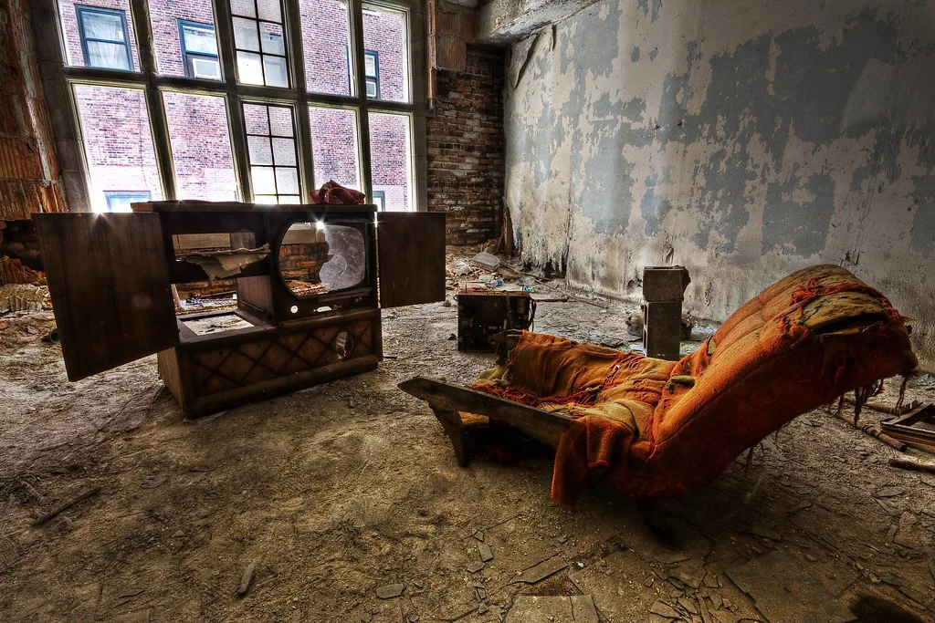 Fauteuil éventré et ancien téléviseur dans une pièce abandonnée aux murs écaillés.