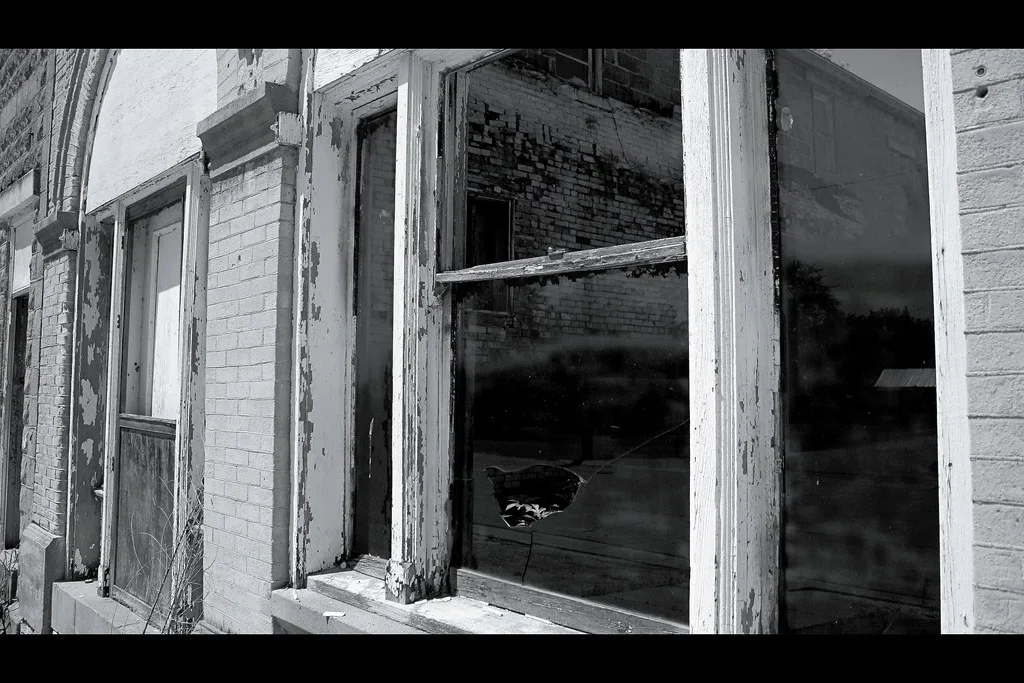 Broken windows with peeling frames on an old brick facade.