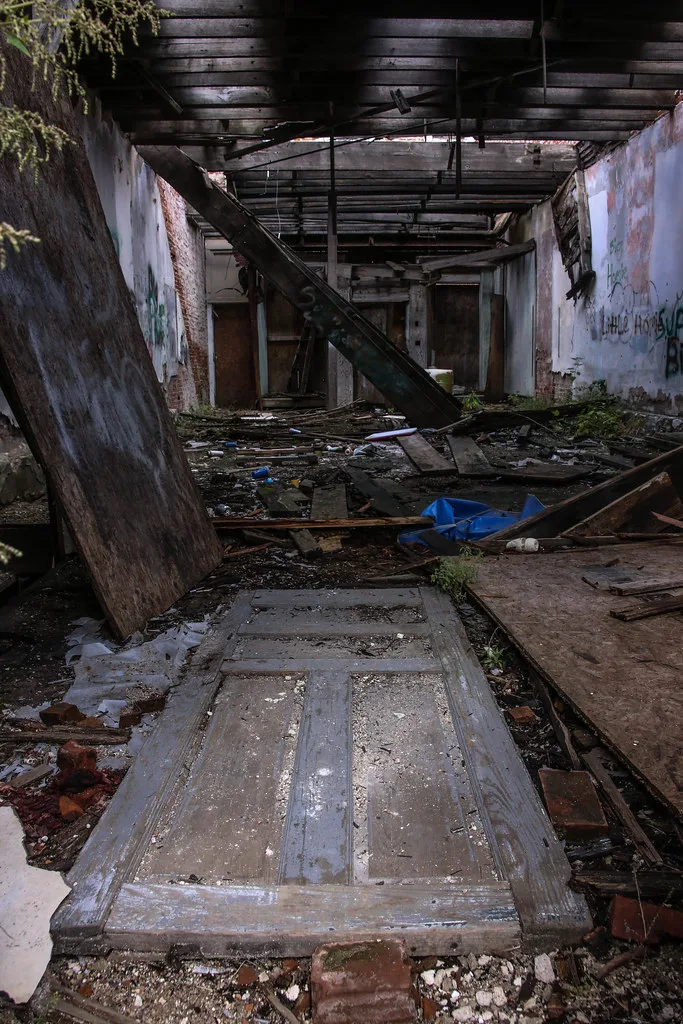 Intérieur en ruine avec une porte au sol et des poutres effondrées.