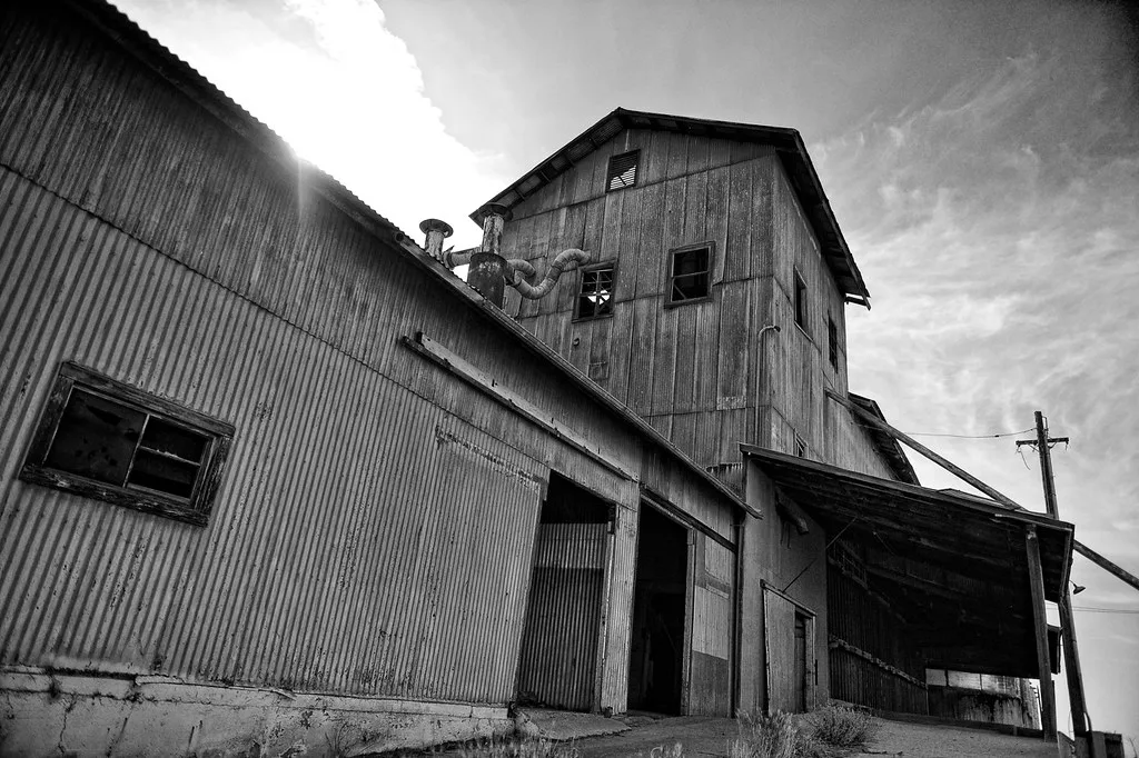 Old corrugated metal industrial building with broken windows, ducts and a large canopy.