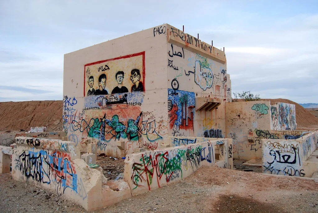 Concrete building remains covered with graffiti in arid ground.