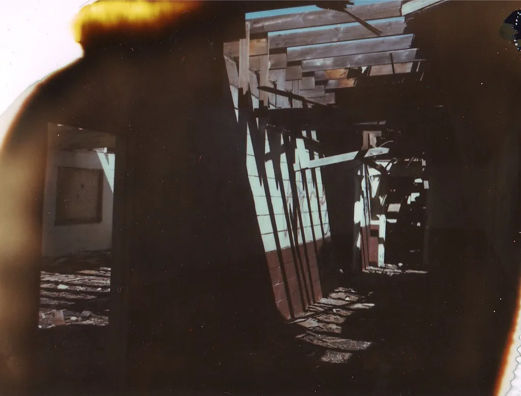 Ruined interior beneath an open roof frame, in a photograph with damaged edges.
