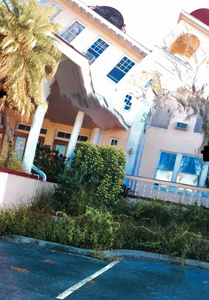 Ancien bâtiment clair aux baies partiellement condamnées derrière une végétation dense.