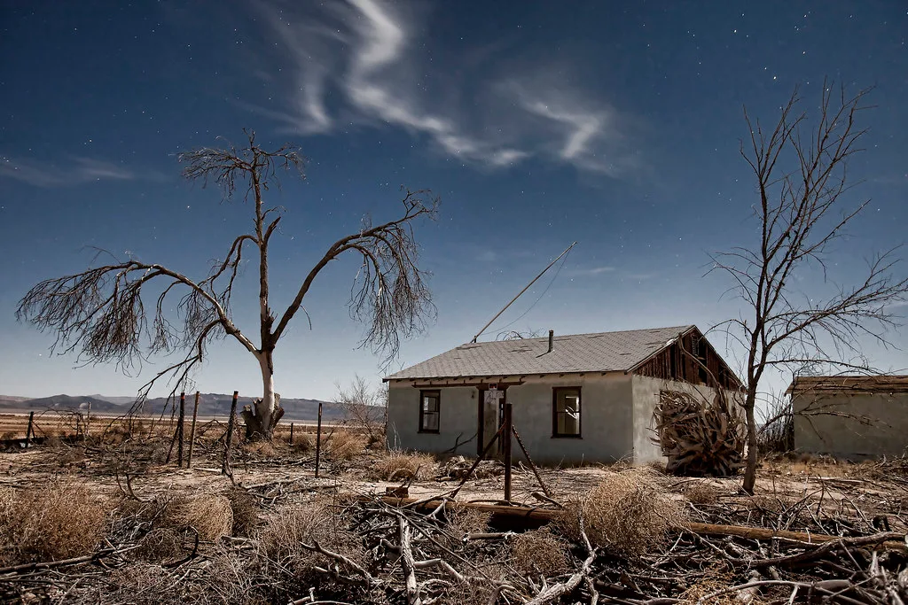 Abandoned house on dry ground, with broken windows and a stripped gable beneath a night sky.