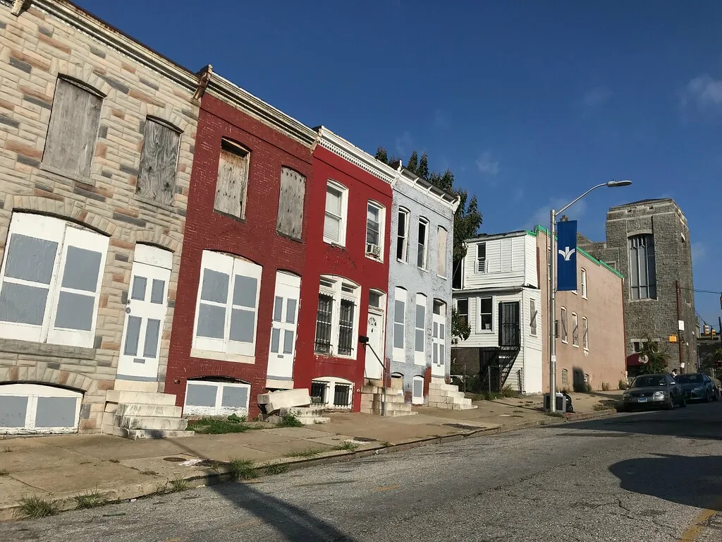 Row houses with boarded windows and doors along a street.