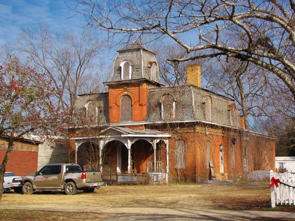 Large brick house with boarded windows and a deteriorated roof.