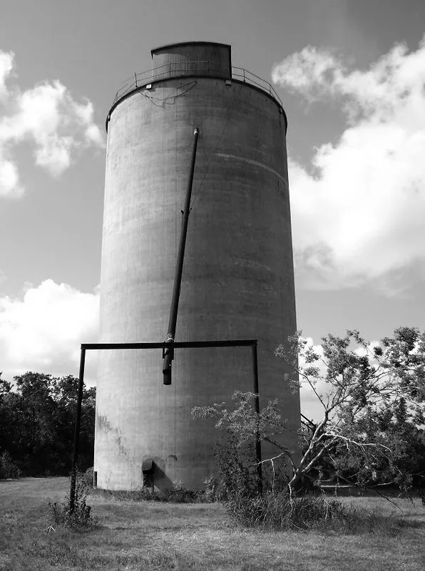 Old cylindrical silo and hanging pipe, in black and white.