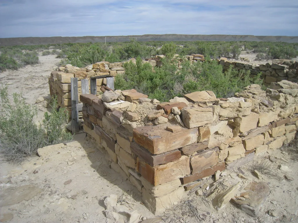 Ruines de murs de pierre remplies de broussailles dans un paysage sec.