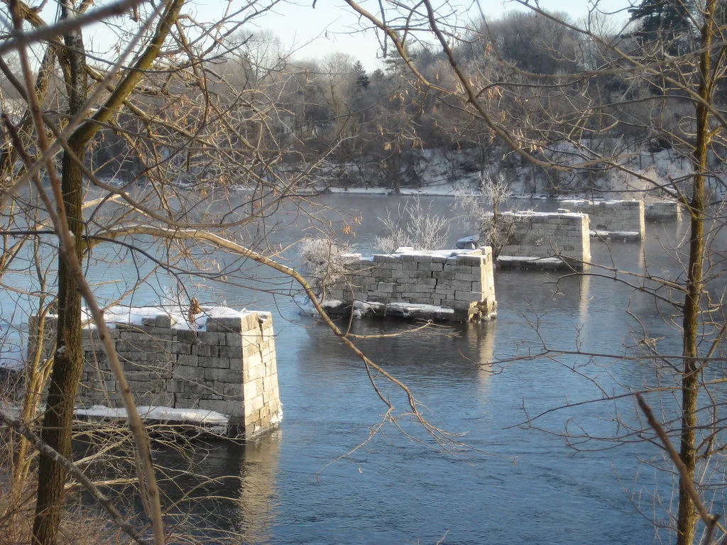 Row of snow-covered stone piers from a former bridge with no deck in a river.