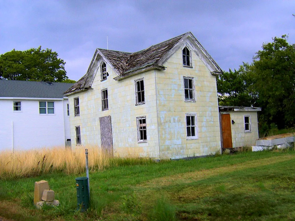 White house with empty windows and a deteriorated roof.