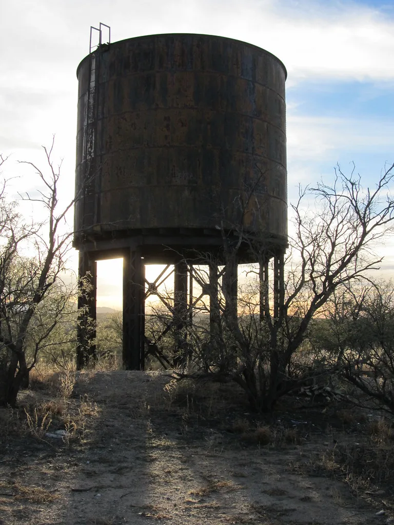 Old rusty metal tank on legs among scrub.
