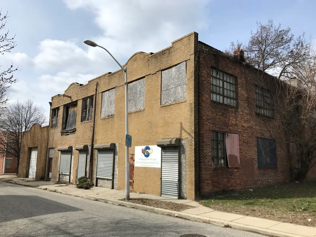 Old yellow brick building with boarded windows and closed metal shutters.