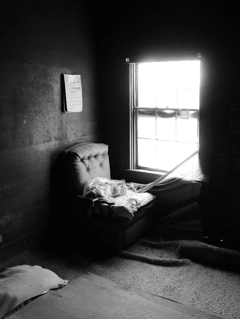 Damaged armchair and fallen blinds in an empty room in black and white.