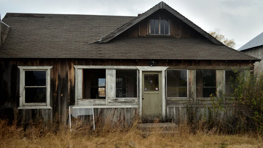 Old wooden house with broken windows behind tall dry grass.