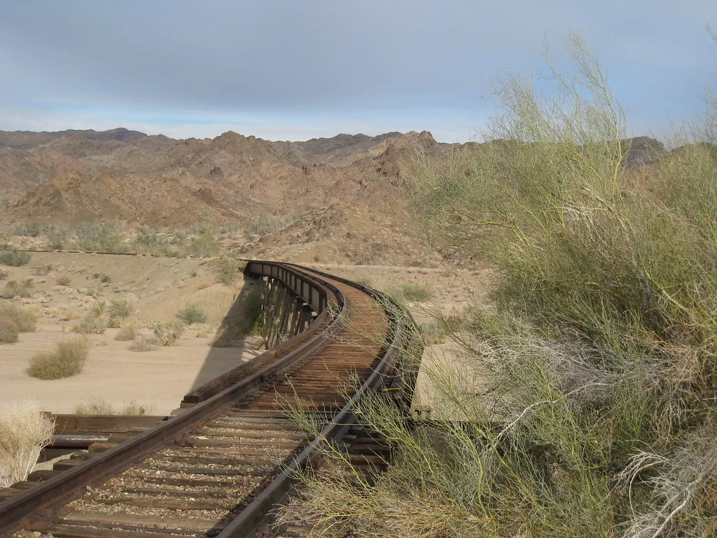 Curving railway track over a wooden bridge in the desert.